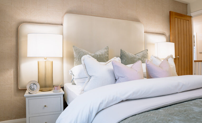 New build bedroom with upholstered headboard and bedside lamp.