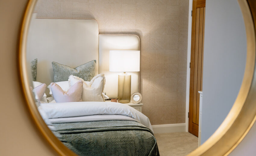 The Tweed new build bedroom with bedside lamp and neutral bedding.