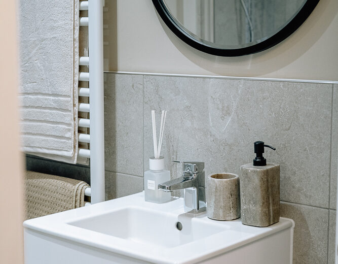 New build bathroom vanity with round mirror and shelf.